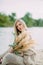 Blonde woman sits on sand beach near lake