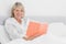 Blonde woman sitting in bed reading smiling at camera