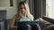 Blonde woman sitting on sofa with laptop on knees using her cell phone