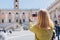 Blonde Woman with smartphone is walking on a sunny day. Capitol in Rome, Piazza del Campidoglio in Capitoline Hill, Rome