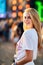 Blonde woman smiles at sunset, enjoying outdoor music event on beach. Crowd gathers behind for live concert experience