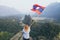 Blonde woman stands on the mountain peak with Laotian flag in her hands overlooking the valley in Vang Vieng, Laos