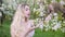 Blonde woman stroking a tree branch with flower buds.