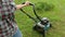 Blonde woman trying to start engine of a lawnmower, summer work in garden, cutting green grass