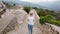 Blonde woman walks on defensive Walls of medieval castle in Europe mountains.