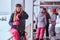 Blonde woman in winter hat and goggles holding a snowboard while sitting on a railing near the snowy sea coast