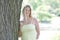 Blonde woman in yellow sundress poses by tree