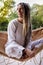 Blonde yogi woman with dreadlocks sitting in a woven hammock.