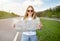 Blonde young lady standing with map on highway, catching ride, hitchhiking on roadside, having autostop trip