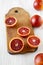 Blood oranges halved on rustic wooden board over white wooden background, side view. Close-up