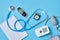 blood pressure monitor, glucometer, stethoscope, notepad and alarm clock on blue background top view