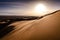 Blowing sand on top of a large sand dune in desert landscape. Early morning sunrise over the desert of Erg Chebbi. Silhouette.