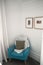 Blue accent chair with brown cushion and the white knitting blanket below the wall paintings