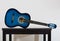 Blue acoustic guitar on a black wooden table isolated on grey wall background. Trendy musical instrument for playing good music.