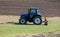 blue agricultural tractor without driver stands on a green meadow in front of a plowed field in the background  sunshine  during