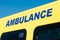 Blue AMBULANCE sign on yellow NHS vehicle.