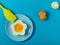 Blue background with egg in a flower shaped bowl and blue plate with broken egg shells and kitchen utensils