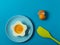 Blue background with egg in a flower shaped bowl and blue plate with broken egg shells and kitchen utensils