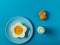 Blue background with egg in a flower shaped bowl and blue plate with broken egg shells and kitchen utensils