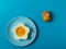 Blue background with egg in a flower shaped bowl and blue plate with broken egg shells and kitchen utensils