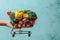 Blue background, hand holds shopping cart filled with fruits and vegetables