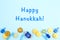 Blue background with multicolor dreidels, menora candles and chocolate coins and Happy Hanukkah wording. Hanukkah and