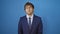 Blue background sets stage for young man, cool yet serious, portrait look. business suit, expressions simple yet strong. confident