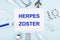 On a blue background, a stethoscope, a thermometer, pills, medicine bottles and a piece of paper with the text HERPES ZOSTER