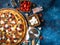 On a blue background on the table lies a pizza beautifully decorated with tomatoes, cheese, olives. Various ingredients are spread
