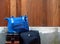 Blue baggage stacked on black large luggage and backpack on wooden and concrete wall background.