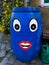 A blue barrel is attached to the house by the gutter. Eyes and mouth are glued to the barrel