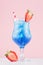 Blue beach cold alcohol drink with curacao liquor, ice cubes, strawberry in elegant wineglass on pastel pink background.