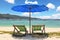 A blue beach umbrella and striped chaise lounges