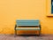 a blue bench sitting against a yellow wall