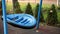 Blue big modern round plastic hanged chain empty swing on children playground at city park or backyard. Green coniferous