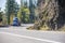 Blue big rig semi truck transporting cargo in covered bulk semi trailer turning around the cliff on the winding road with autumn