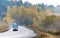 Blue big rig semi truck transporting container on winding autumn road in raining weather