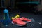 A blue bottle, crimson sneakers, a mobile phone with headphones, two yellow dumbbells on a dark blurred background.