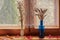 A blue bottle with ears of rye and a small crystal vase with ears of oats stand on a wooden windowsill