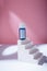 Blue bottle of serum or acid with blank label, care cosmetics container mock up template on white concrete stairs, pink backdrop