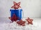 A blue bucket with star pattern filled with white paper shreds and 3 red wooden stars on a plaster background, for 4th of July,