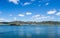 Blue calm deep water lake with small island surrounded by hills with trees under a blue sky with small soft white clouds.