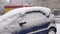 Blue car, covered with a thick layer of snow.  It`s snowing outside