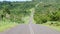 Blue car driving down empty asphalt road running past dense tropical vegetation