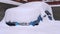 A blue car under a thick layer of snow. a lot of snow