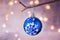 Blue Christmas tree ball with snow flake ornament hanging on branch. Shining garland golden lights.