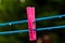A blue clothing line with many raindrops at the string in front of a dark background, with a pink peg after the rain. Retro way o
