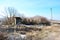 Blue cloudy sky above the meadow with abandoned ruined brick house and trees without leaves, dry grass and melting snow