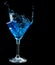Blue cocktail splashing into glass on black