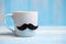Blue coffee cup with Black mustache on wood table background in the morning. Father, International men day, Prostate Cancer